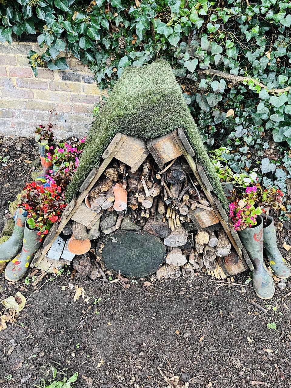 A small insect hotel made from wood, hollow stems and stacked logs between painted boots