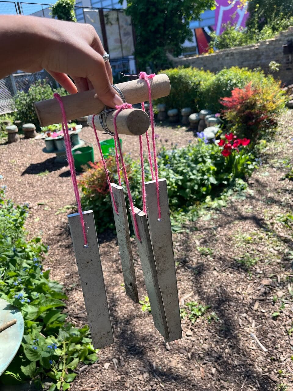 A handmade wind chime with metal pieces hanging on pink string